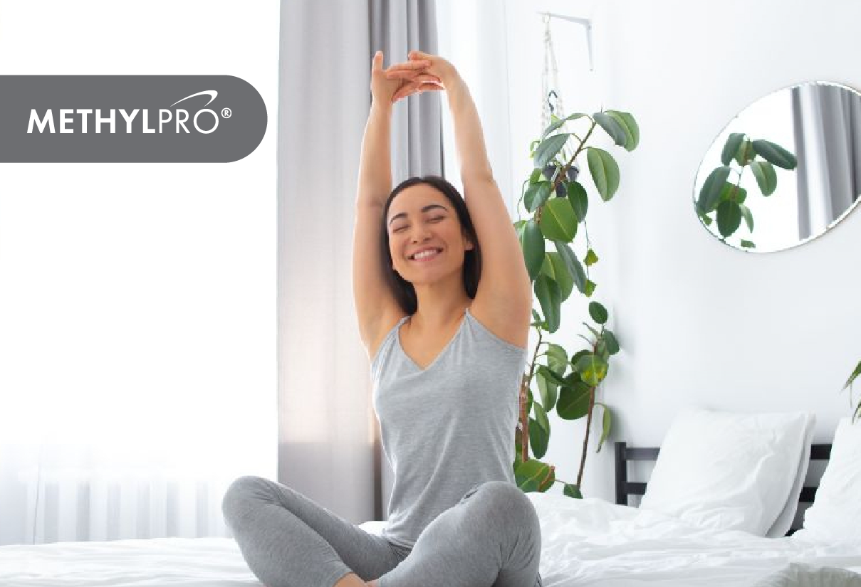 Woman stretches on a bright bedroom bed with a leafy plant nearby and MethylPro branding.