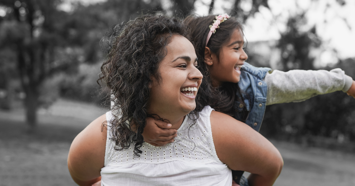 Mother giving her daughter a piggyback ride in a park.