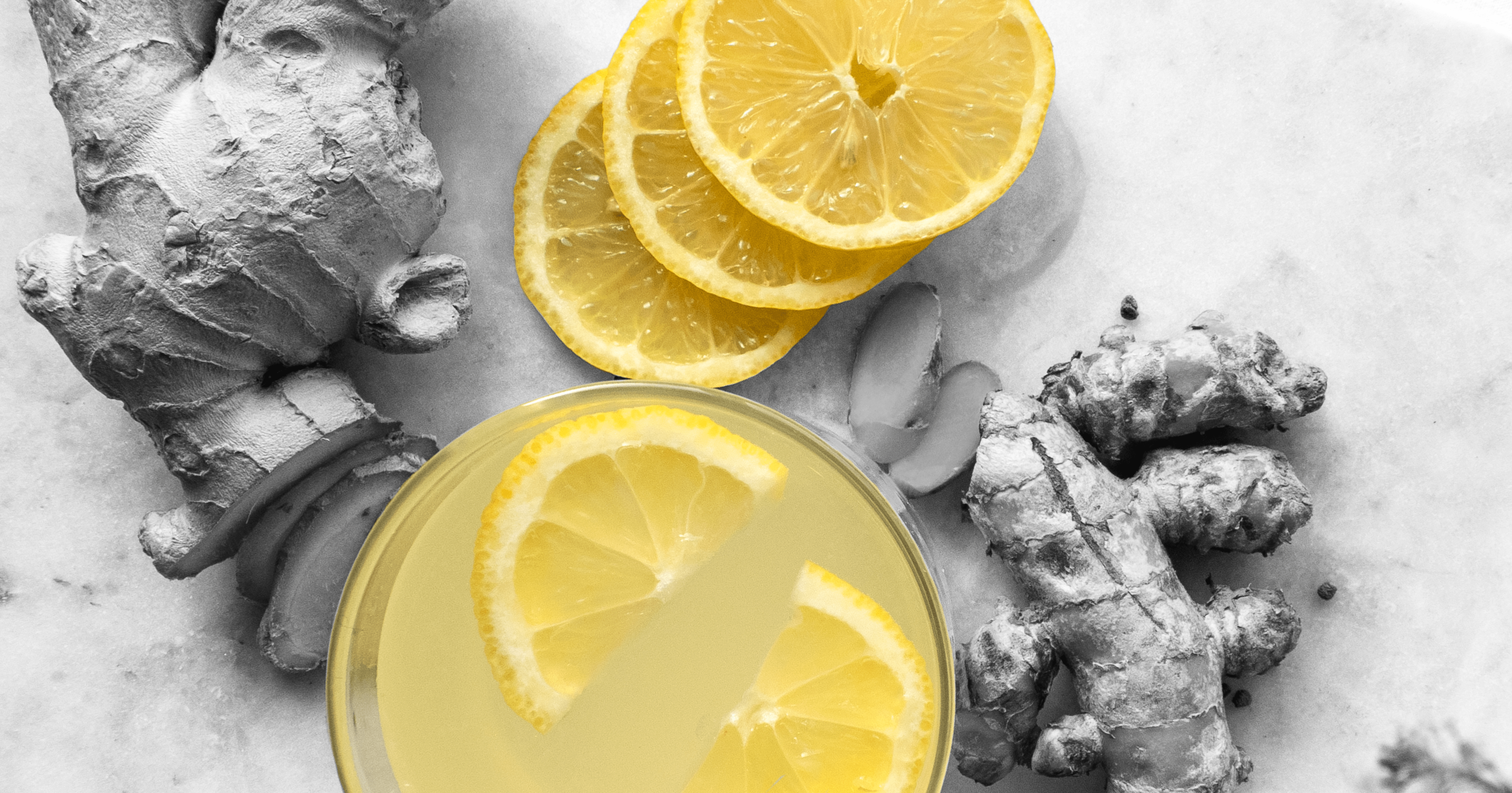 Top view of lemon slices, ginger roots, and a glass of lemonade with lemon wedges.