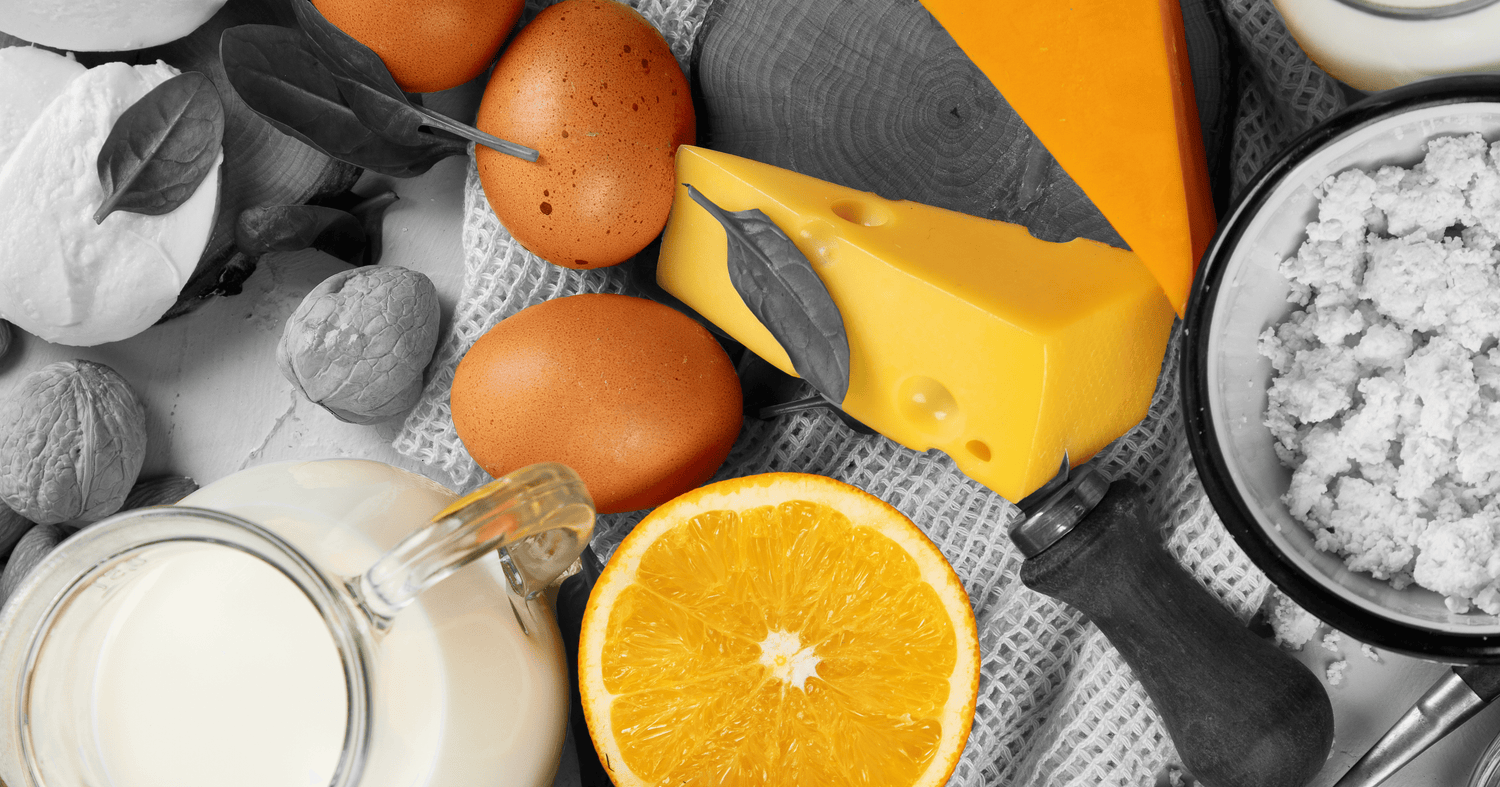 Assorted protein rich foods including cheese, eggs, milk, nuts, and a halved orange arranged on a textured cloth