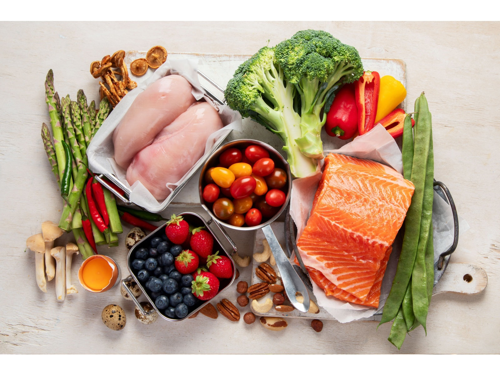 Colorful whole foods for mental health featuring salmon, chicken, broccoli, peppers, berries, and nuts on a wooden board.