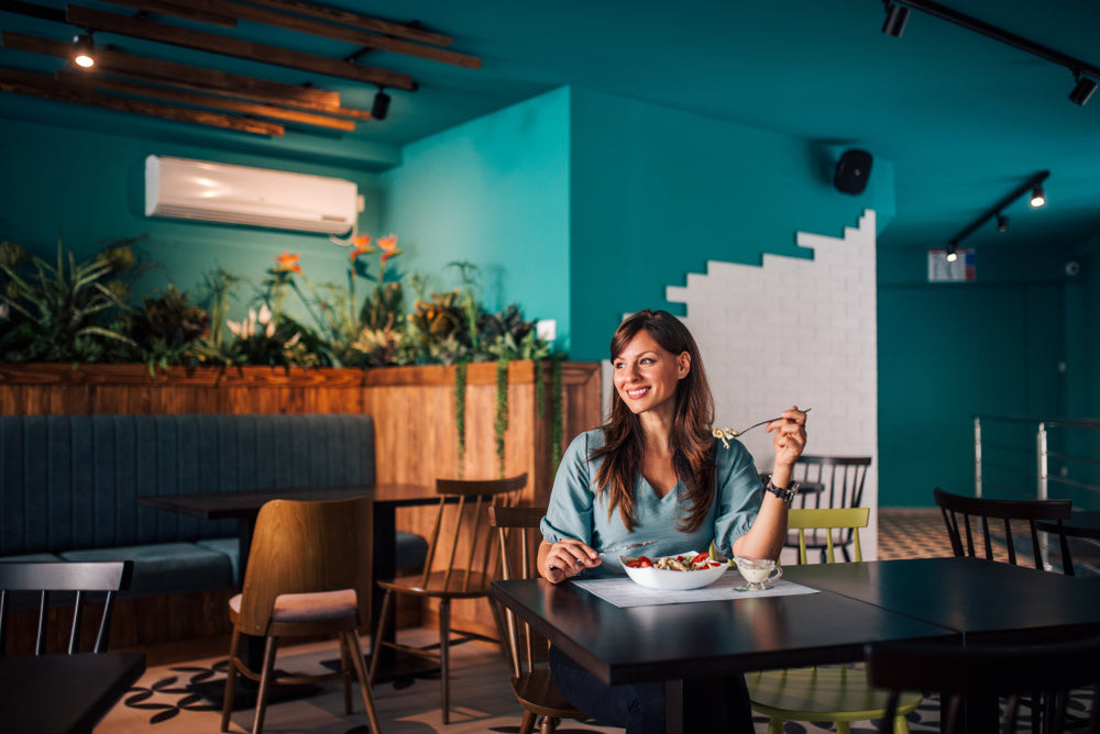 Woman in teal top sits at a modern cafe table eating a salad.