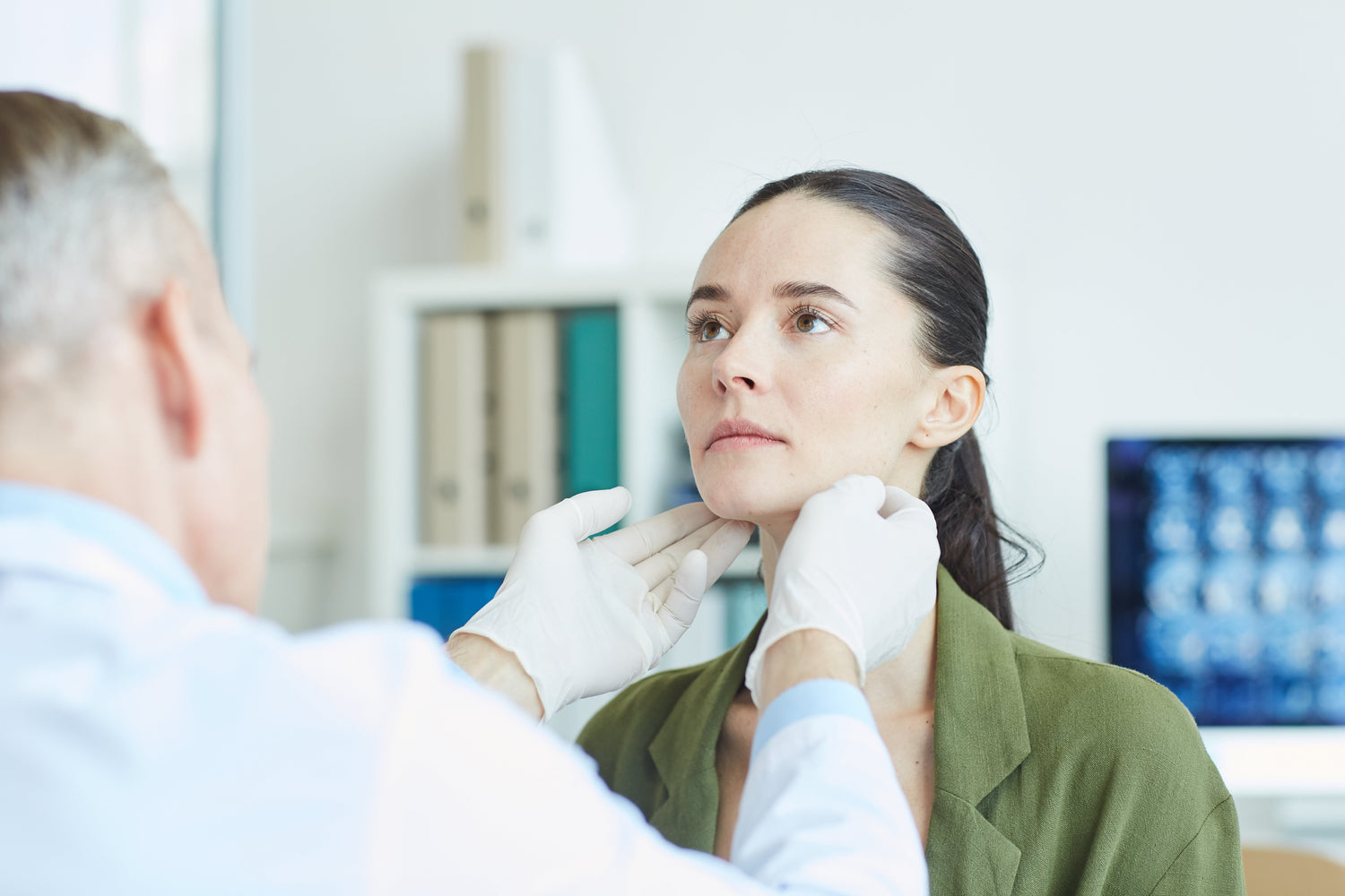 Medical professional palpating a woman's neck to examine the thyroid.