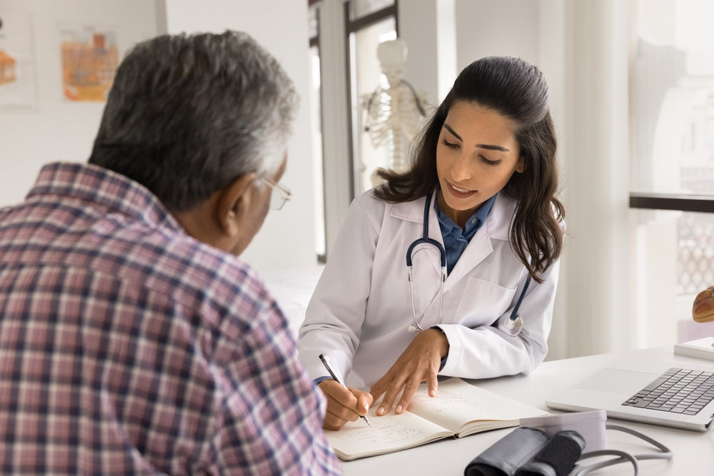 Female physician with a stethoscope consults an elderly patient at a desk.