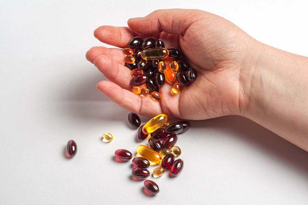 Hand cupping assorted soft gel capsules in amber and dark red, representing dietary adrenal glandular supplements.