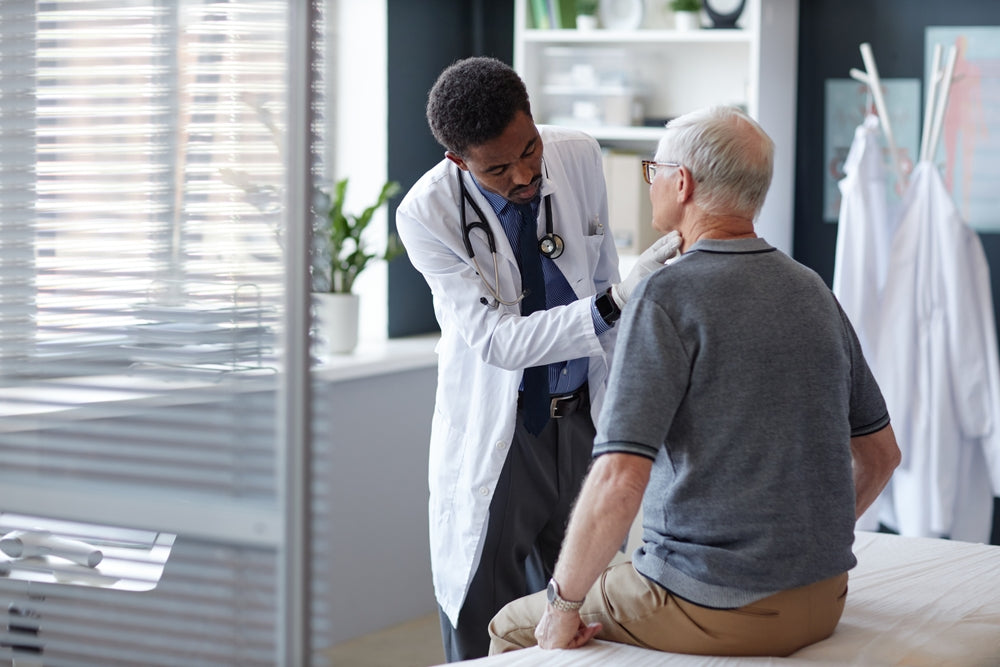 Physician in a white coat listens to an elderly man's chest with a stethoscope during a clinic exam