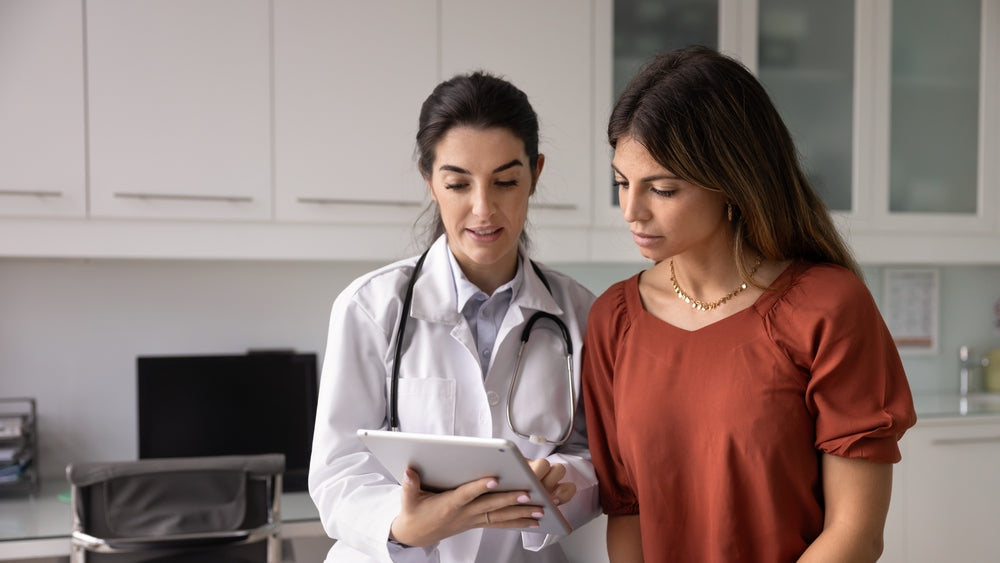 Female doctor with stethoscope explains tablet information to a patient in a modern clinic.