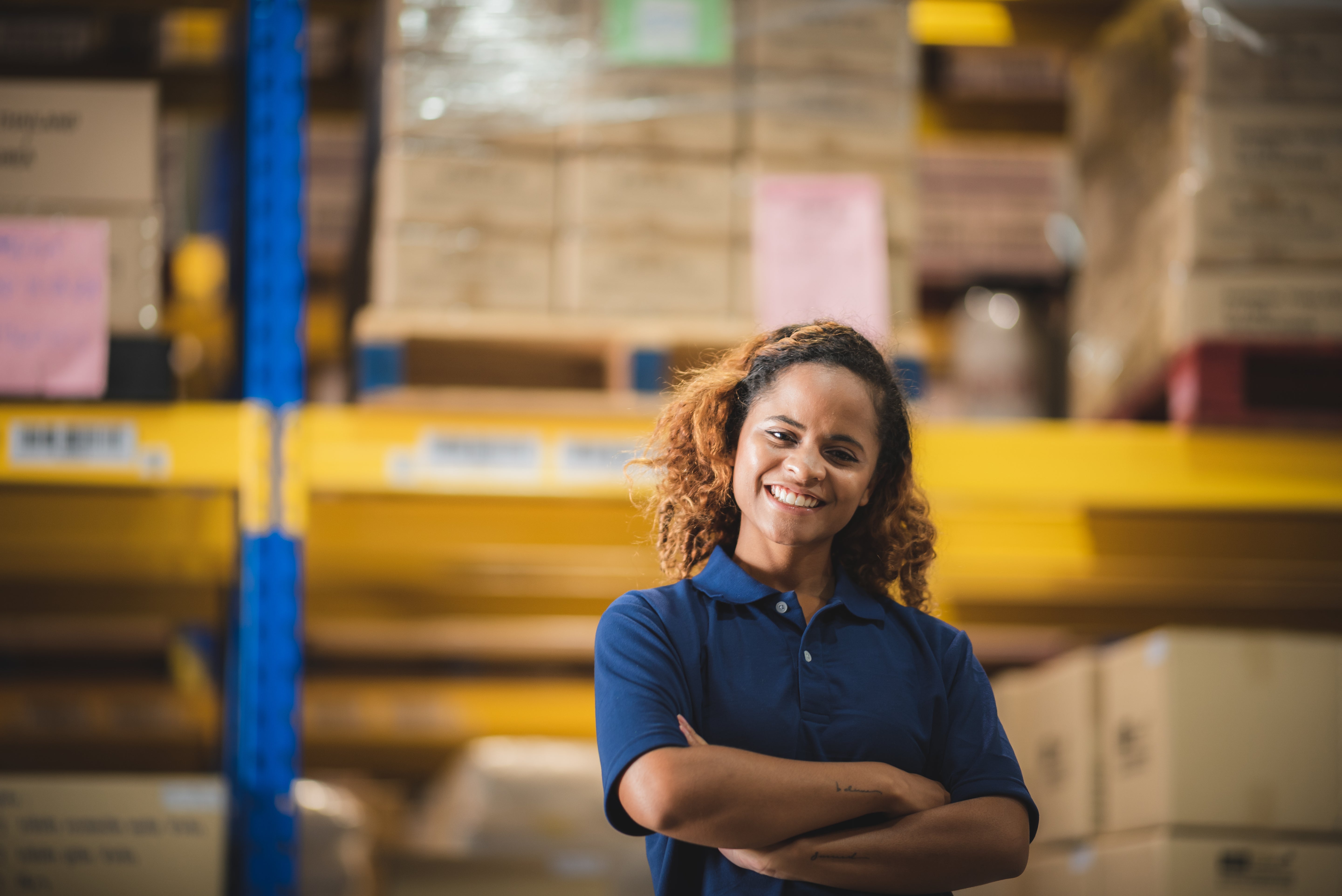 Woman standing in a warehouse with arms crossed, smiling.