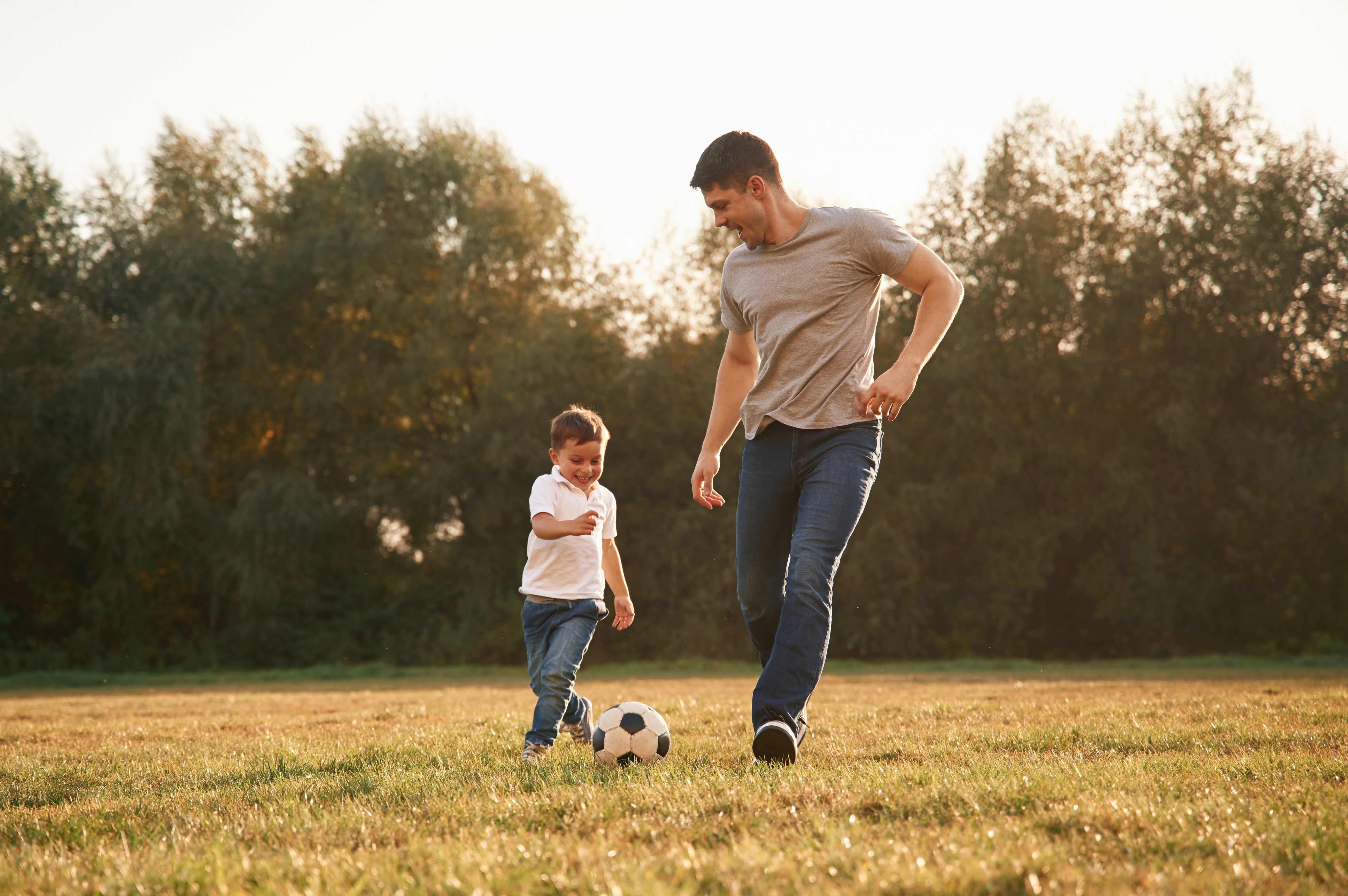 Man and child playing with a soccer ball on a grassy field