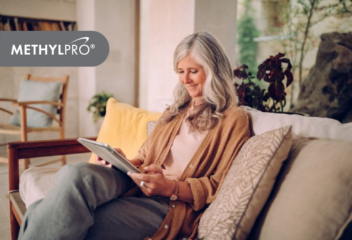 Older woman relaxing on a sofa reading a tablet in a bright living room.