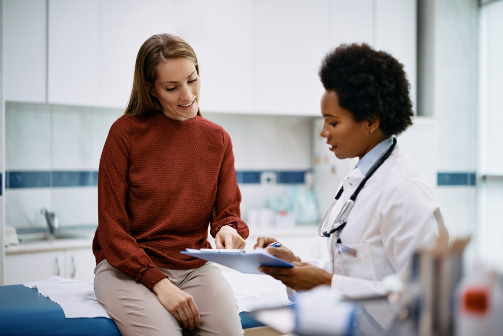 Female doctor with a stethoscope discusses with a patient in a red blouse in a bright exam room