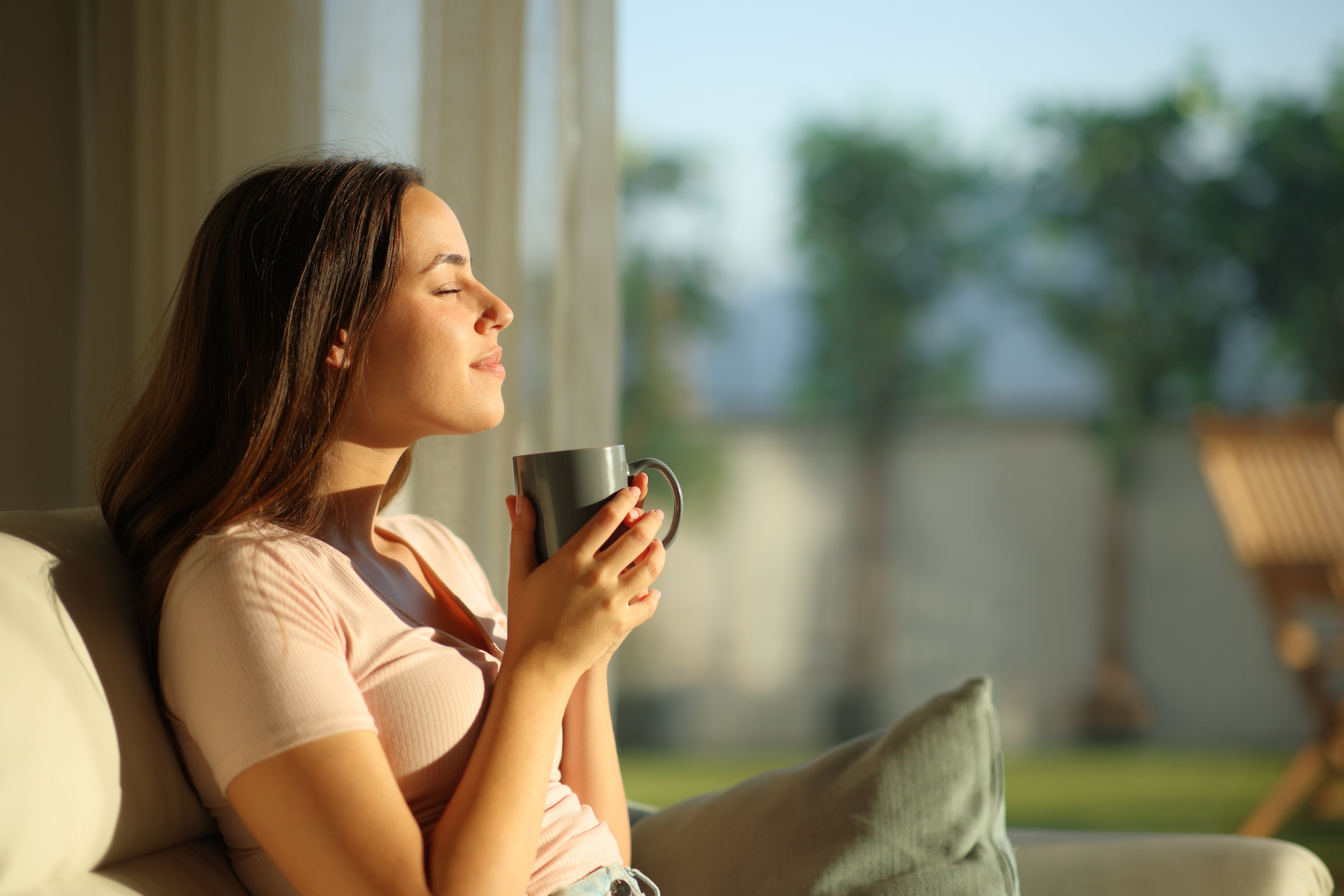 Woman holding a mug, sitting on a couch with a blurred outdoor background